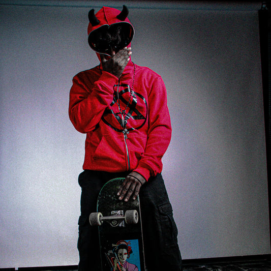 Person wearing a red hoodie and black pants holding a skateboard with a white background